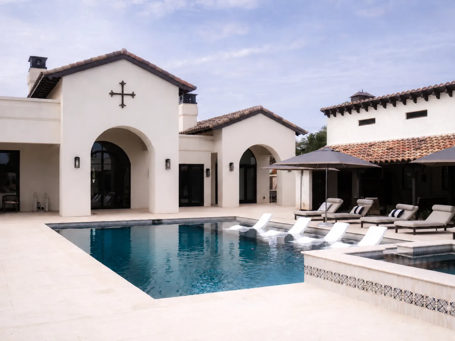 Completed Spanish-style luxury residence with arched entry opening onto a swimming pool and shaded outdoor living area